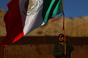 A man waves a Mexican flag during a binational Mass on Saturday at the U.S.-Mexico border in memory of migrants who died during their journey to the United States.